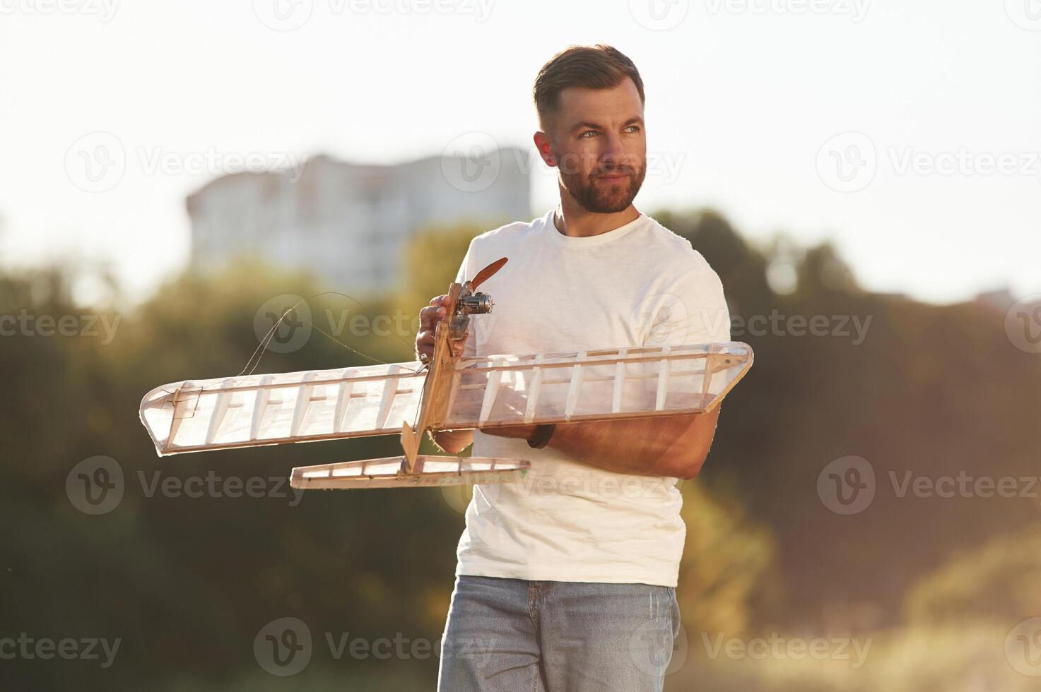 In casual clothes. Man is on ,the, field ,fixing the toy plane photo
