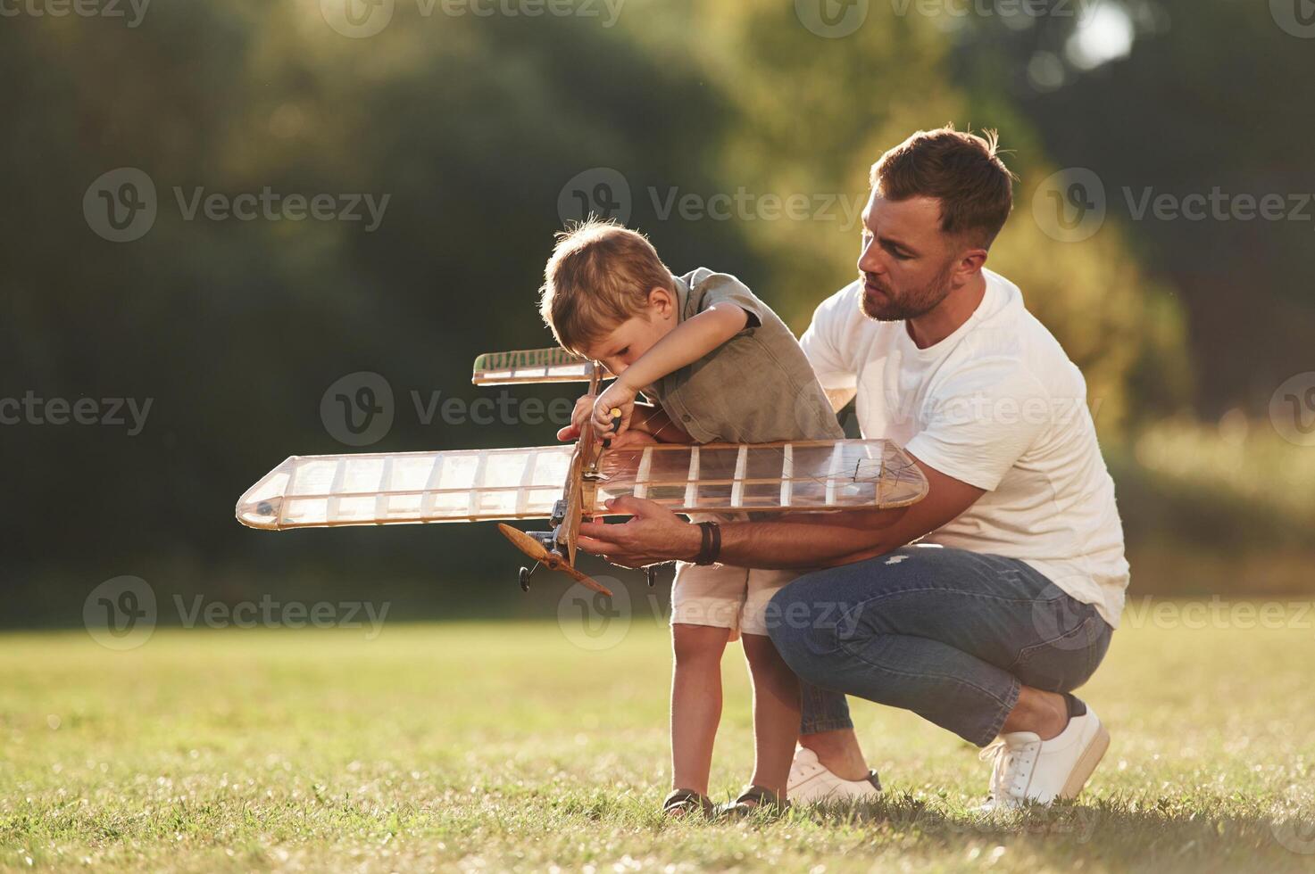 Trying to fix it with screwdriver... Father and son are on the field together with toy plane photo