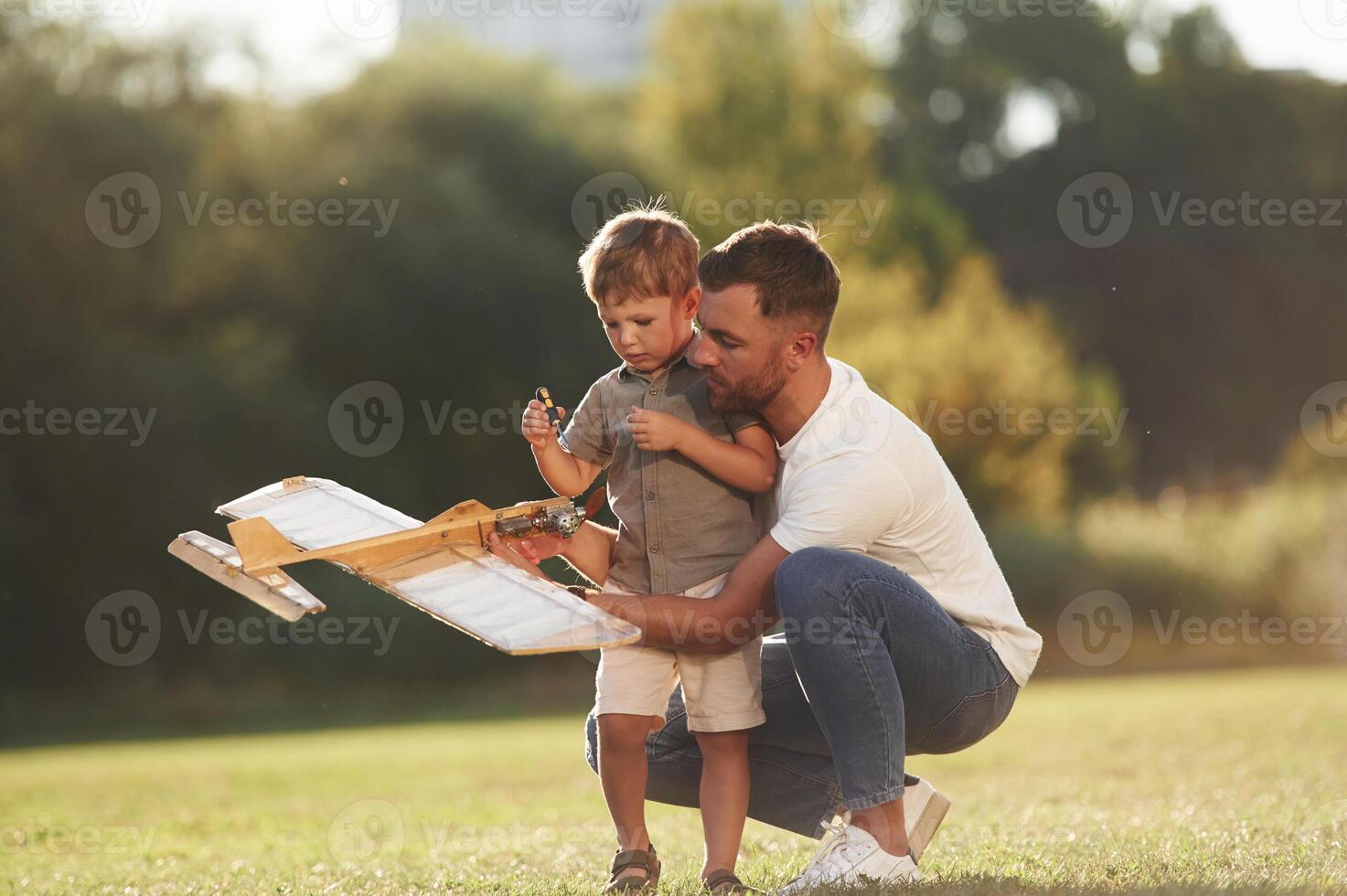 Trying ,to,,, fix it with screwdriver. Father ,and son are on the field together with toy plane photo