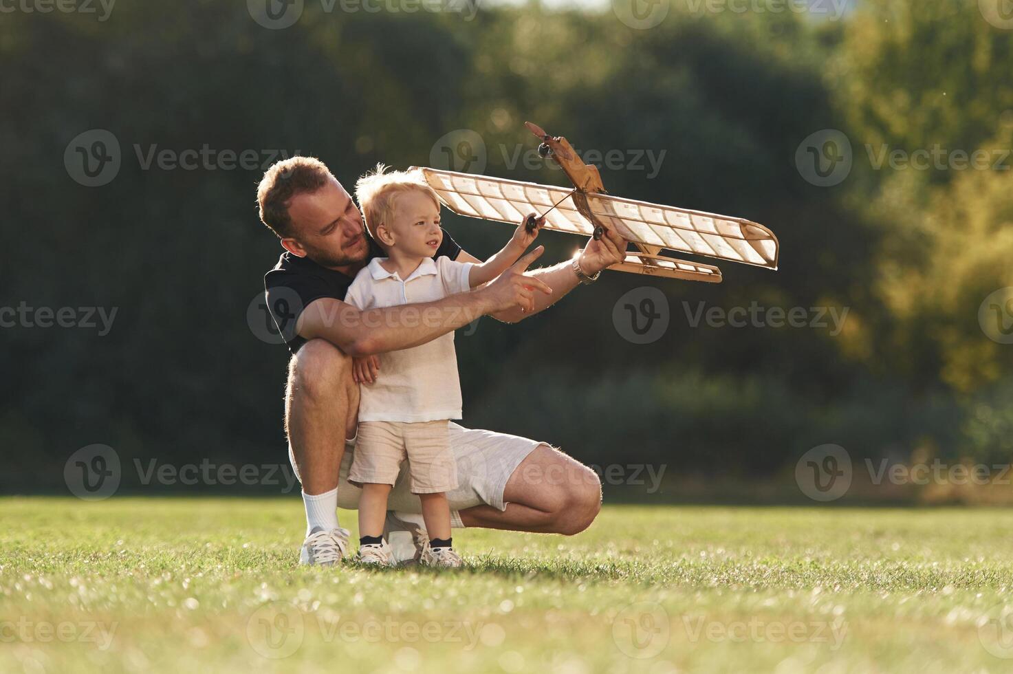 Screwdriver in ,,hand, fixing it. Father and son are on the field together with toy plane photo