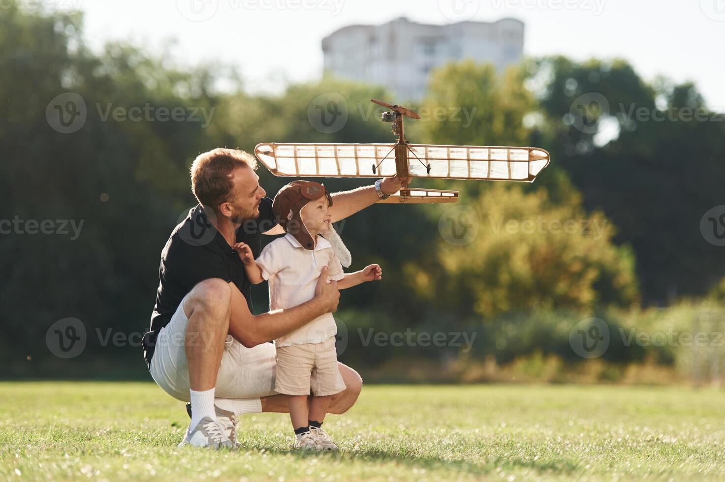 Having fun, sitting. Father and son ,are ,on ,the field together with toy plane photo