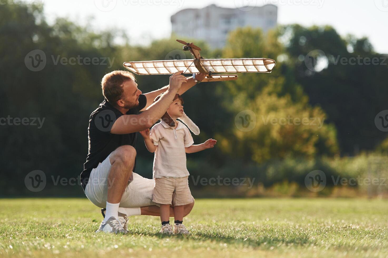 Having fun,, sitting,. Father, and son are on the field together with toy plane photo