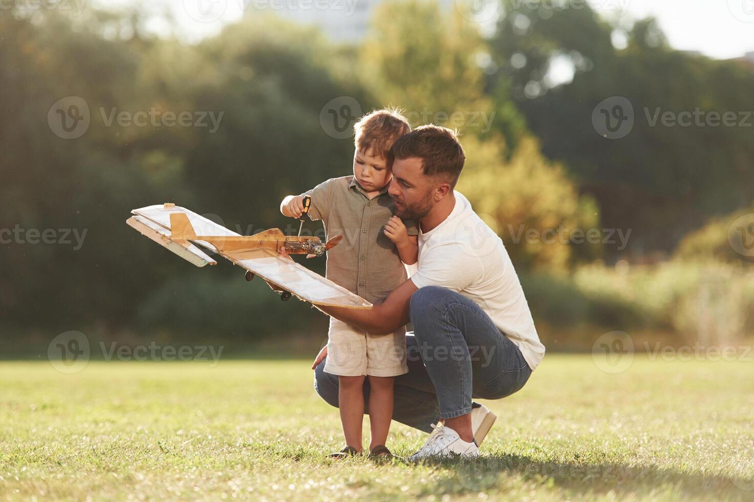 Trying, to, fix it with,, screwdriver. Father and son are on the field together with toy plane photo