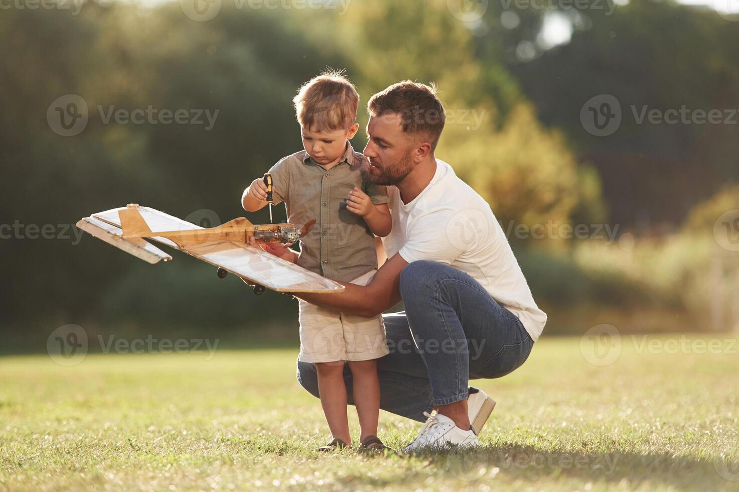 Trying, to, fix ,it with screwdriver. Father and son are on the field together with toy plane photo