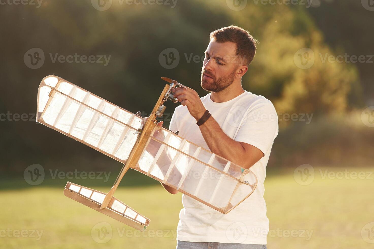 In ,casual clothes. Man is on the field fixing the toy plane photo