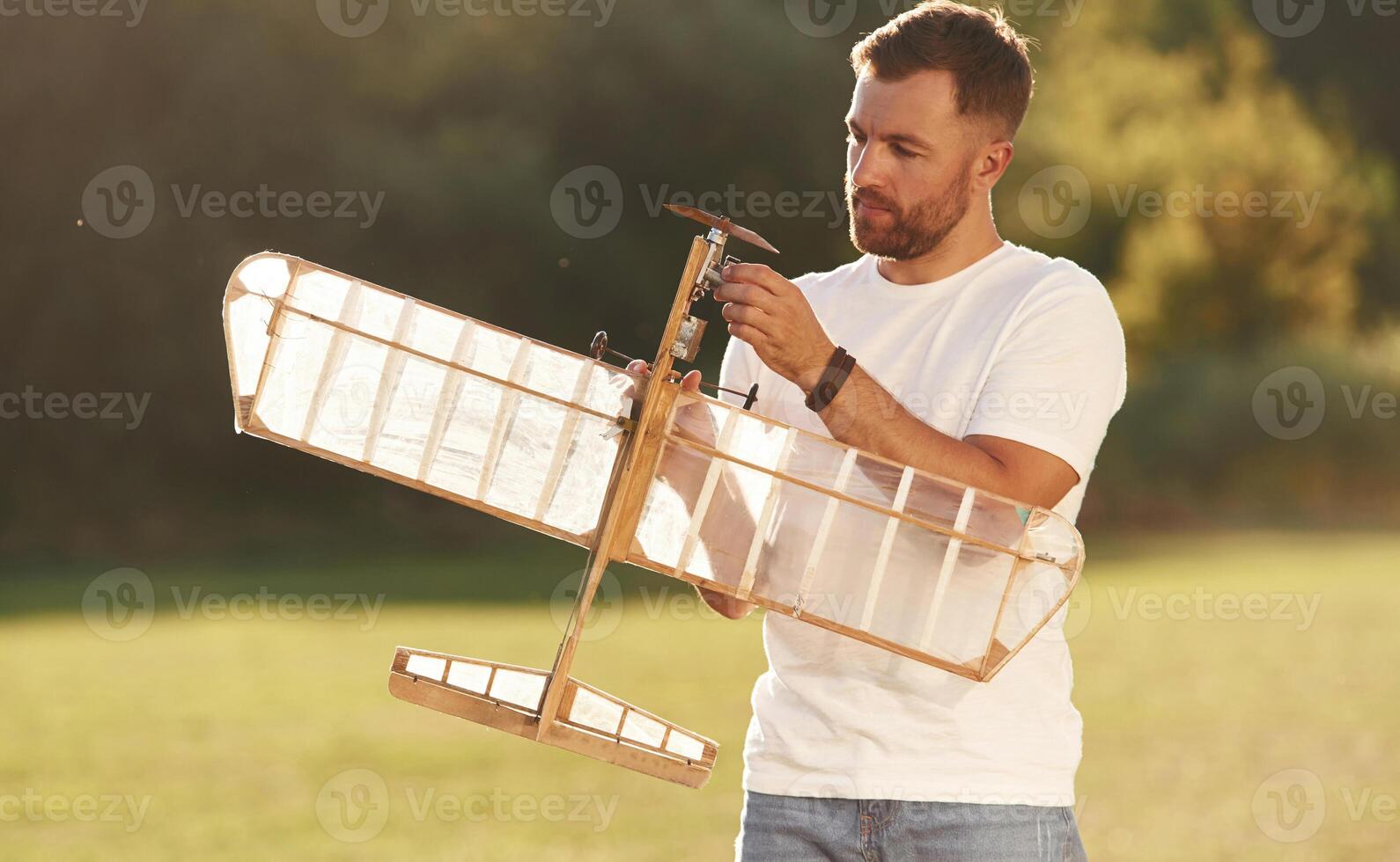 In, casual clothes. Man is on the field fixing the toy plane photo
