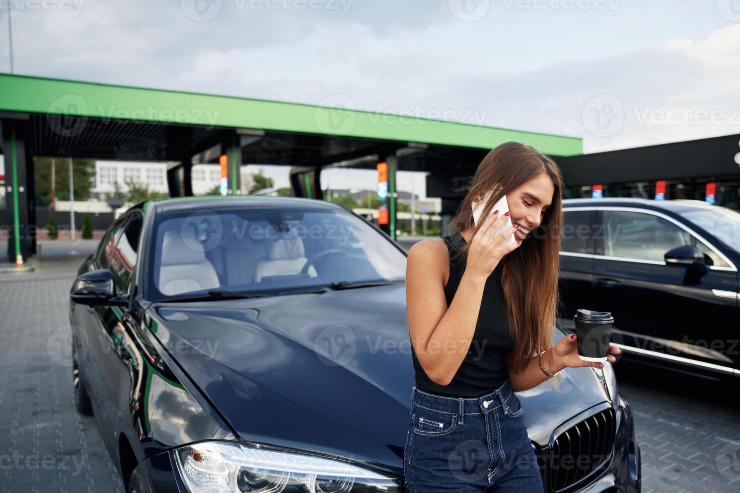 Happy conversation ,by,, phone. A young woman at a gas station with her car photo