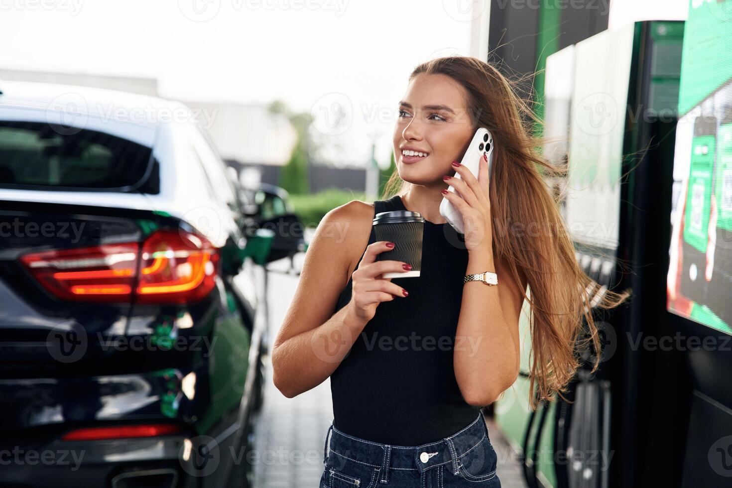 Having a conversation by phone. A young woman at a gas station with, her car photo