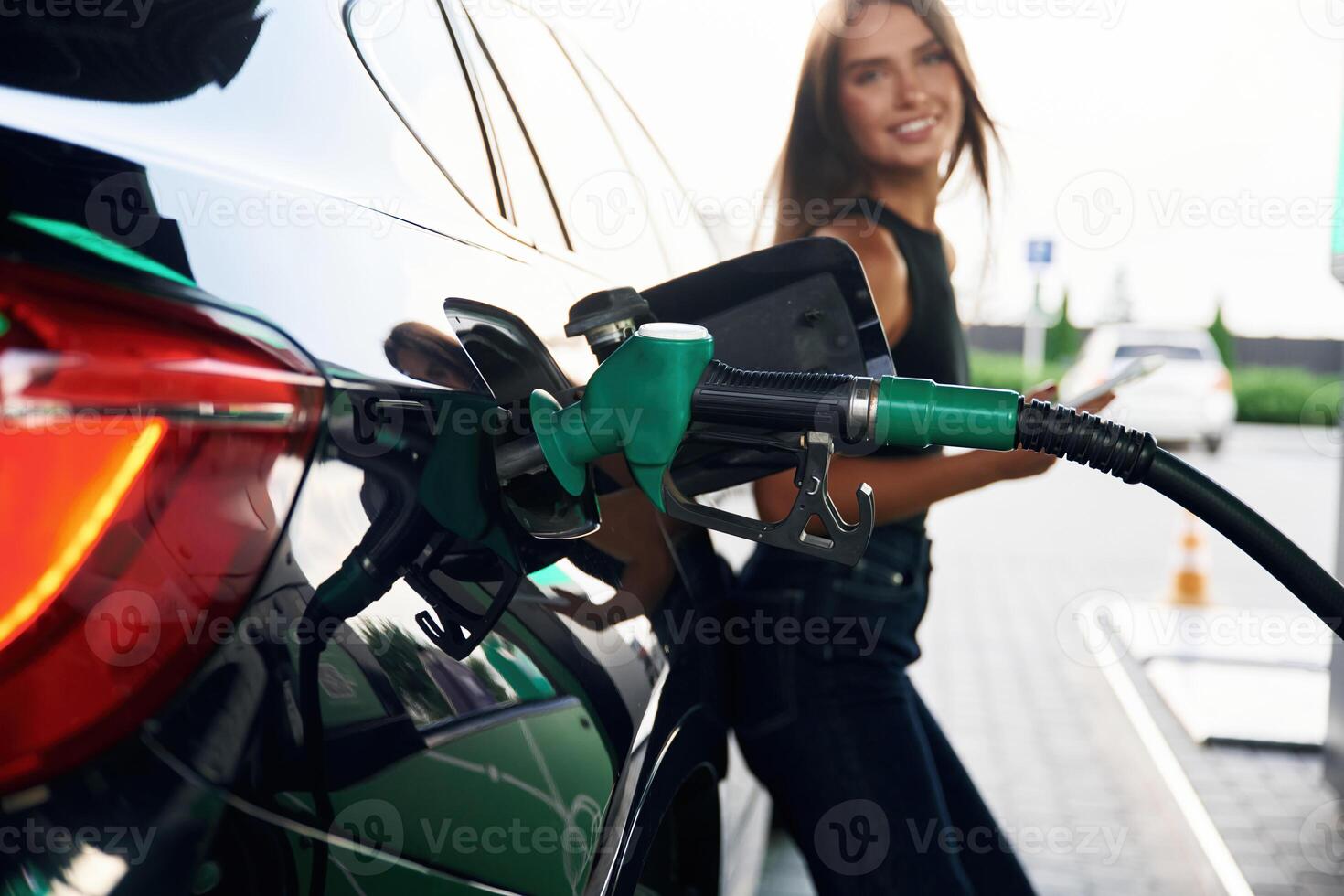 Waiting, holding ,smartphone. A ,young ,,woman at a gas station with her car photo