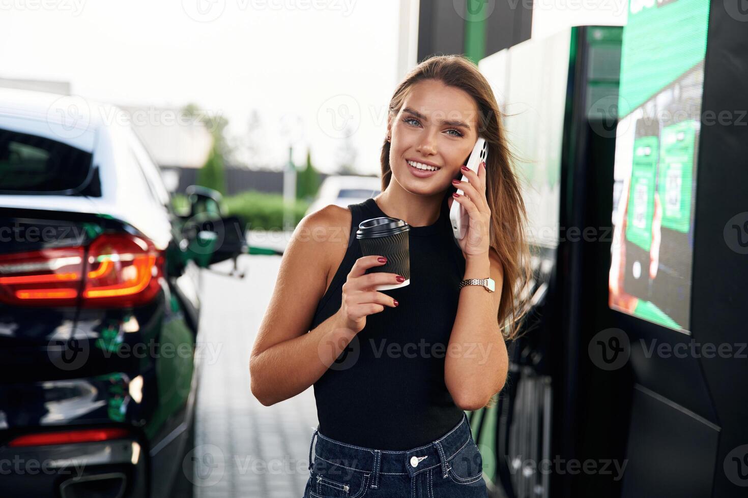 Having ,a, conversation by phone. A young woman at a gas station with her car photo