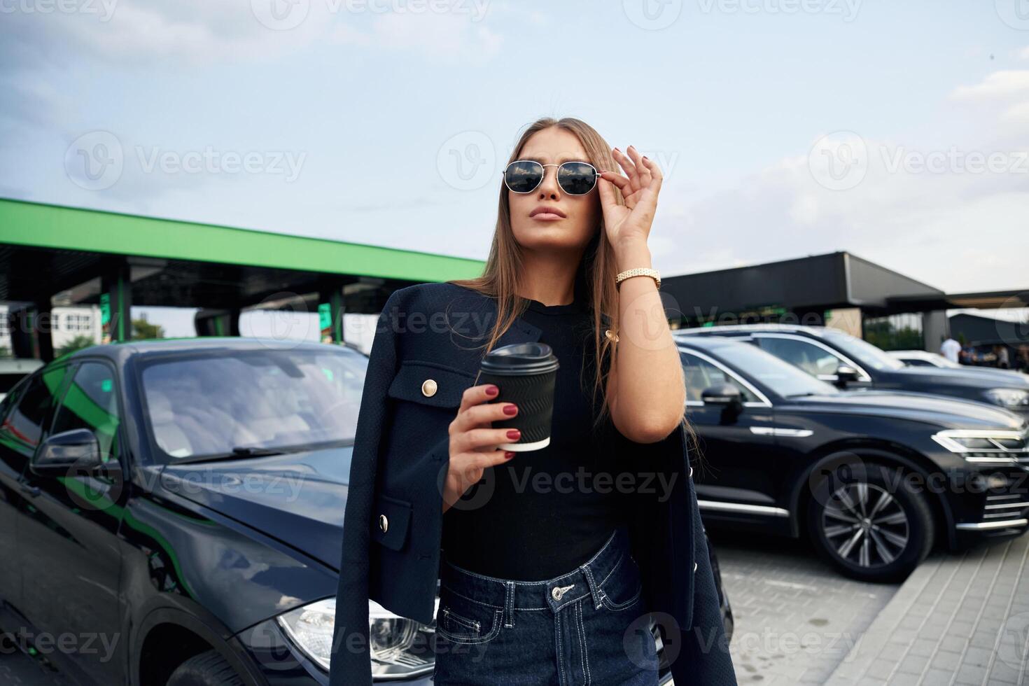 In sunglasses.. A young woman a,t a gas station with her car photo