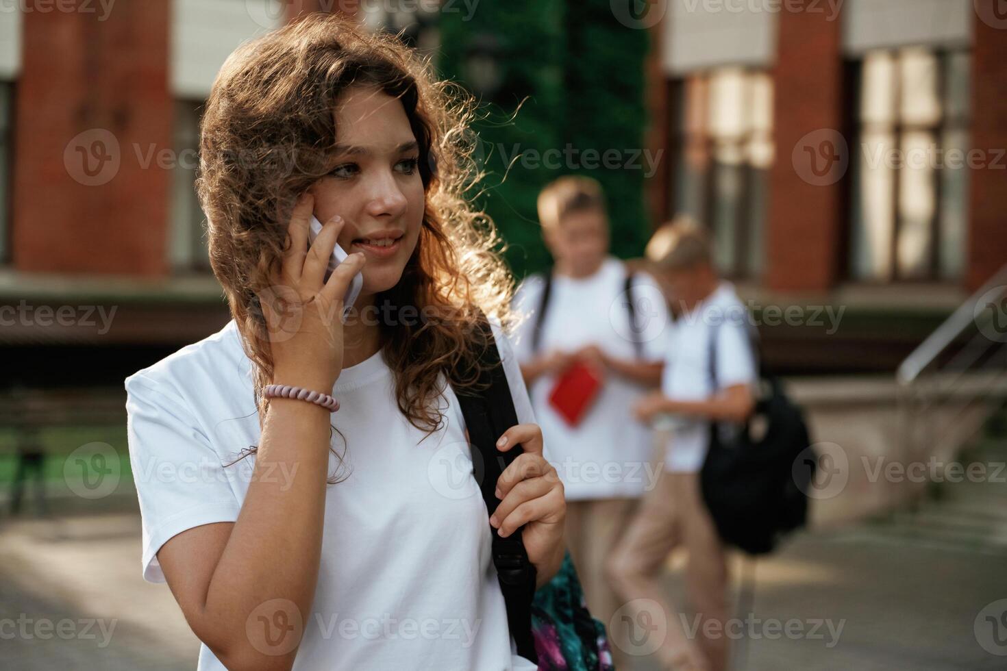 Girl is talking ,by, phone. Kids are near the school together, pupils photo