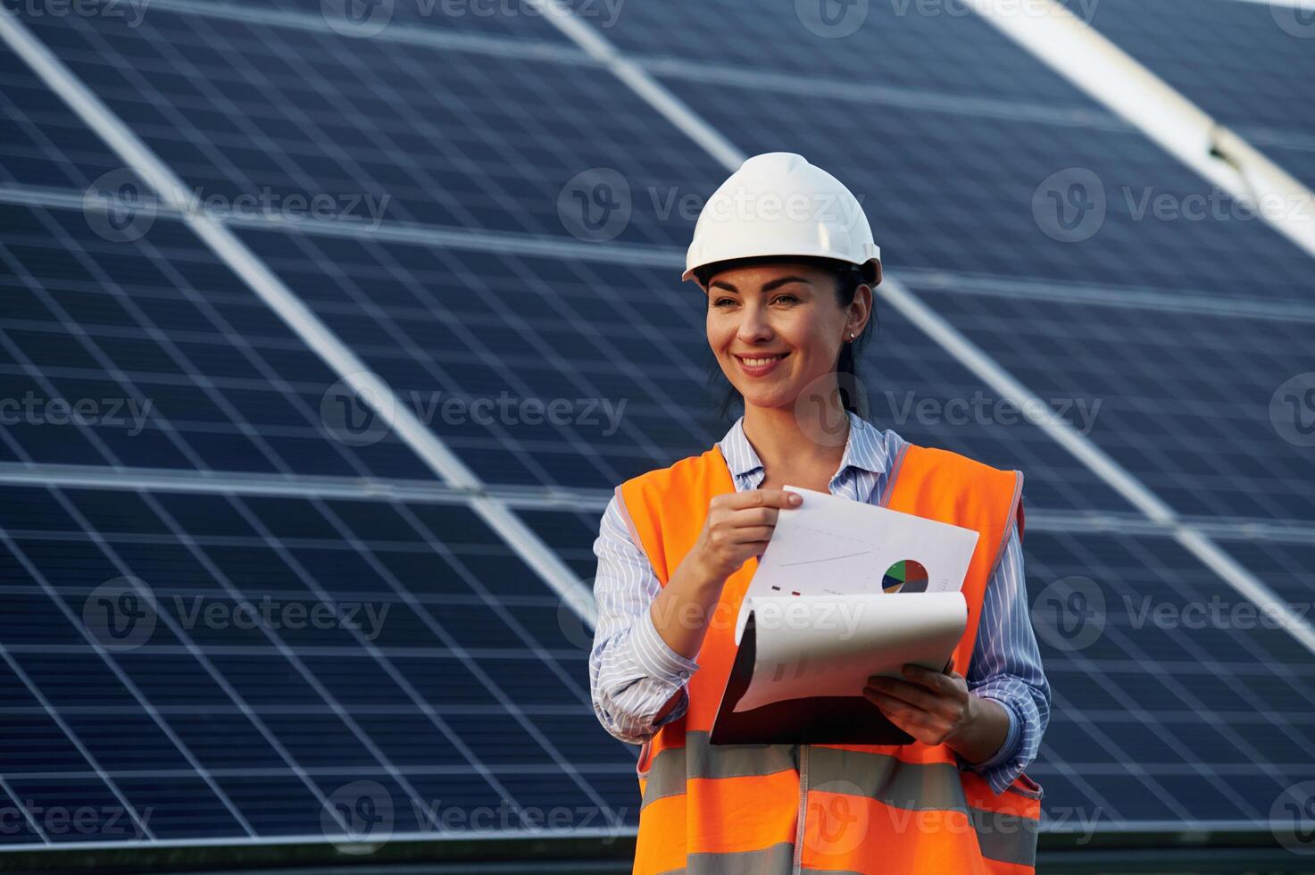 Notepad in hands. Female worker engineer in, uniform is near solar panels.. photo