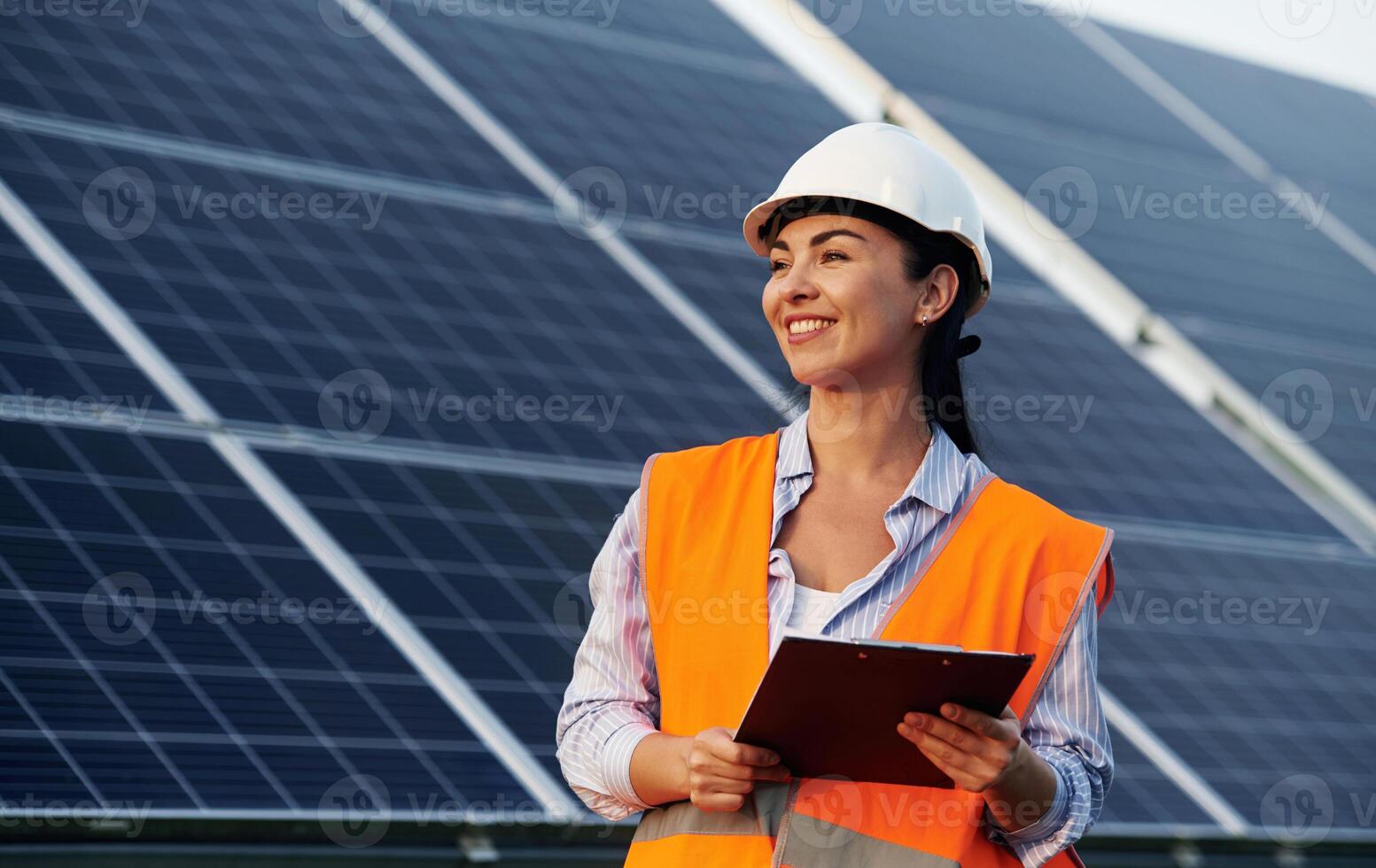 Notepad in hands. Female worker engineer in uniform is near solar panels. photo