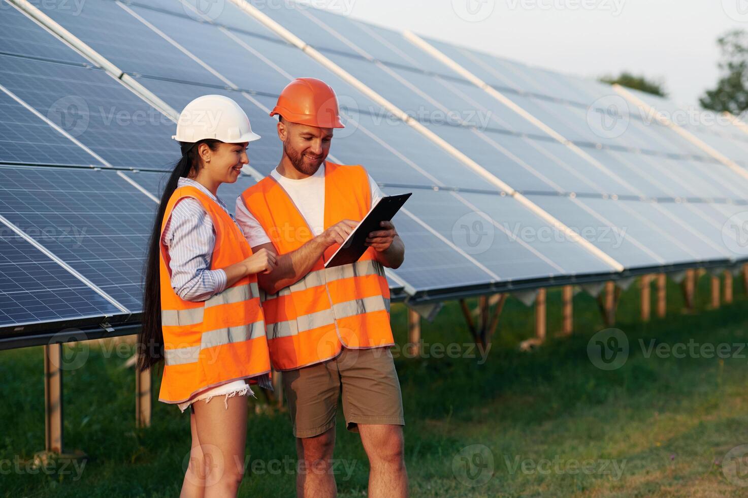 Reading the information from notepad. Man and woman, workers are near solar panels,. in uniform photo