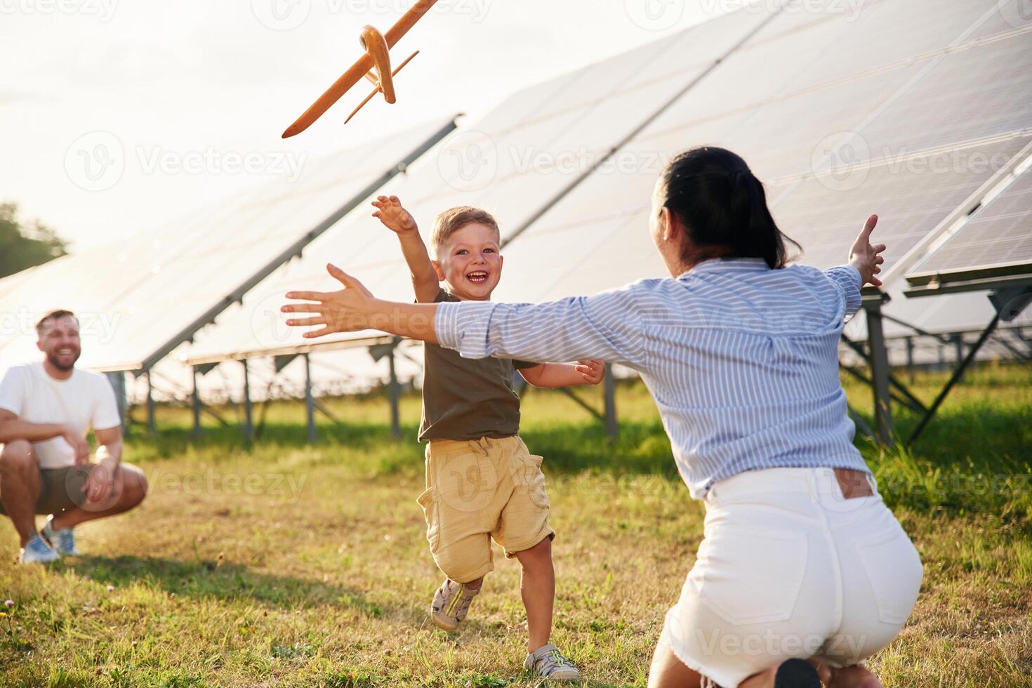 Running, to ,a ,,parent with toy plane. Father, mother and little son are outdoors near solar panels photo