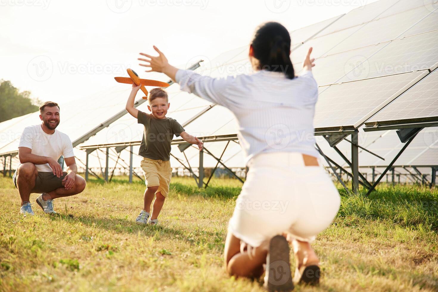 Running to a ,parent ,with toy plane. Father, mother and little son are outdoors near solar panels photo