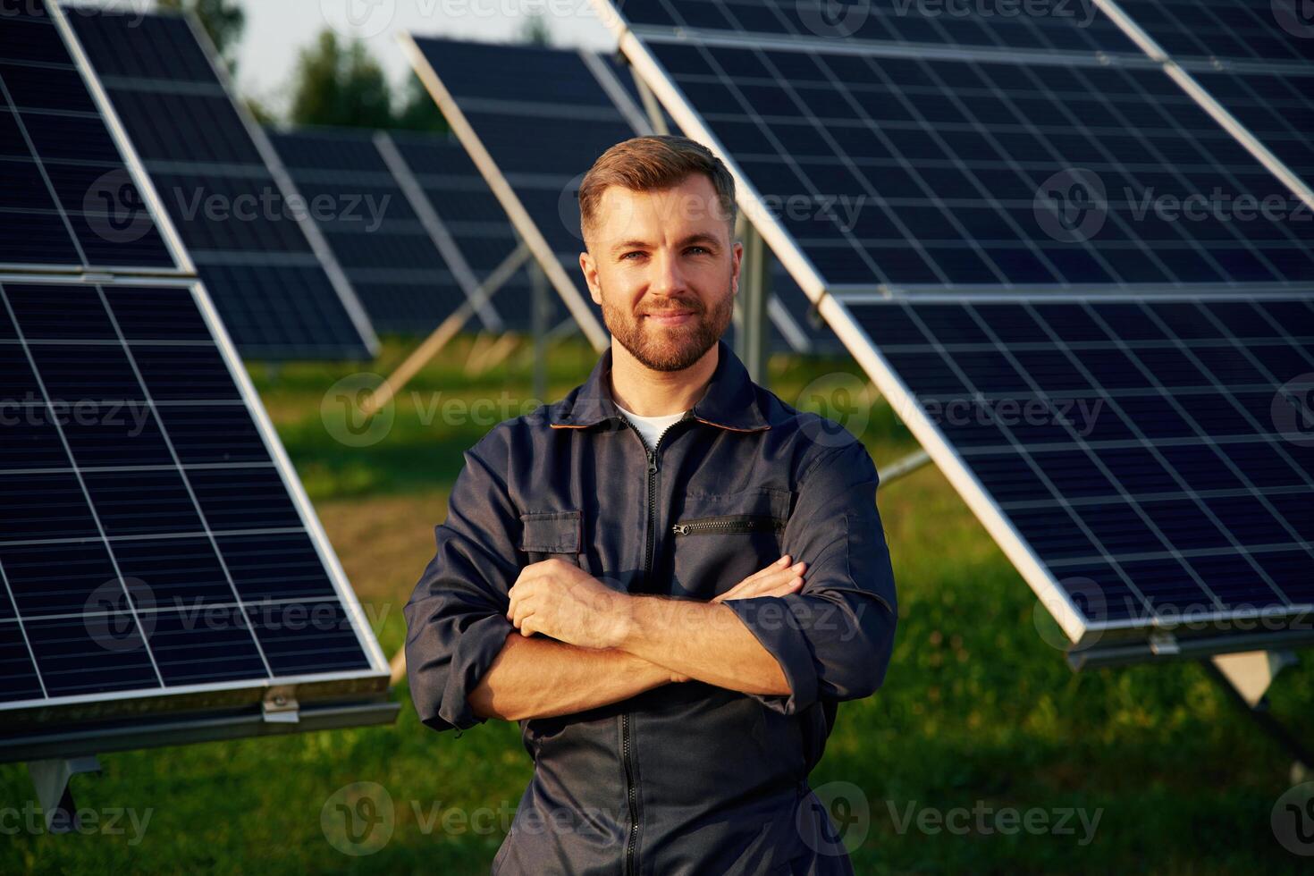 Portrait, standing,,,, with arms crossed. Man is working with solar panels outdoors at daytime photo