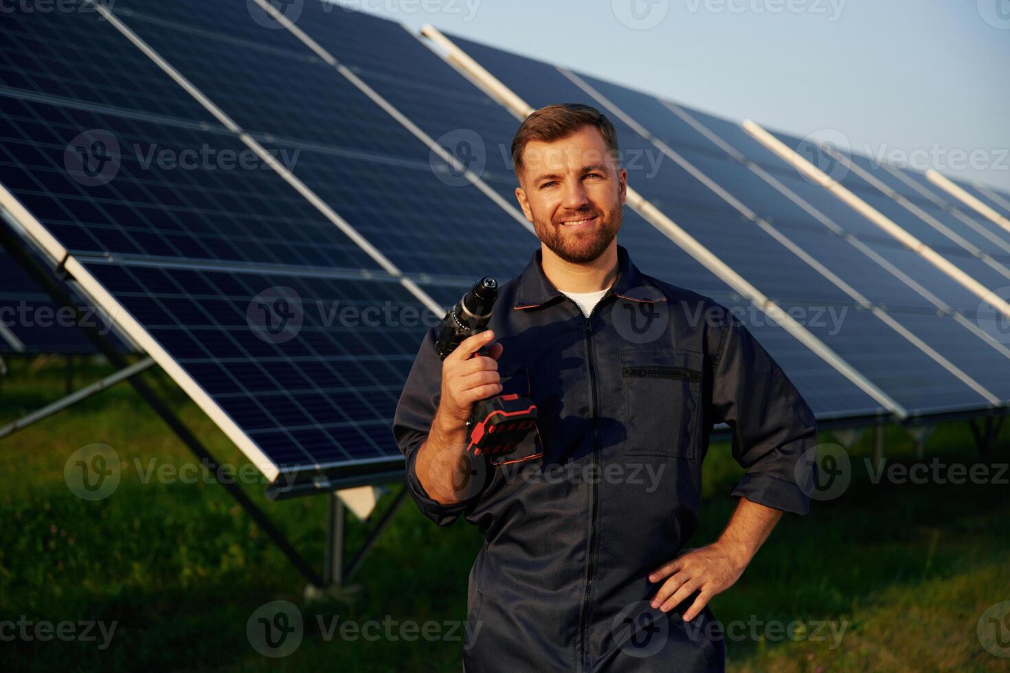 Outside, standing and, holding ,the drill. Man is working with solar panels outdoors at daytime photo