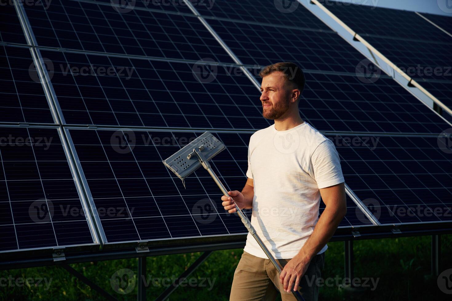 Mop in hands. Man is working ,with solar panels outdoors at daytime photo