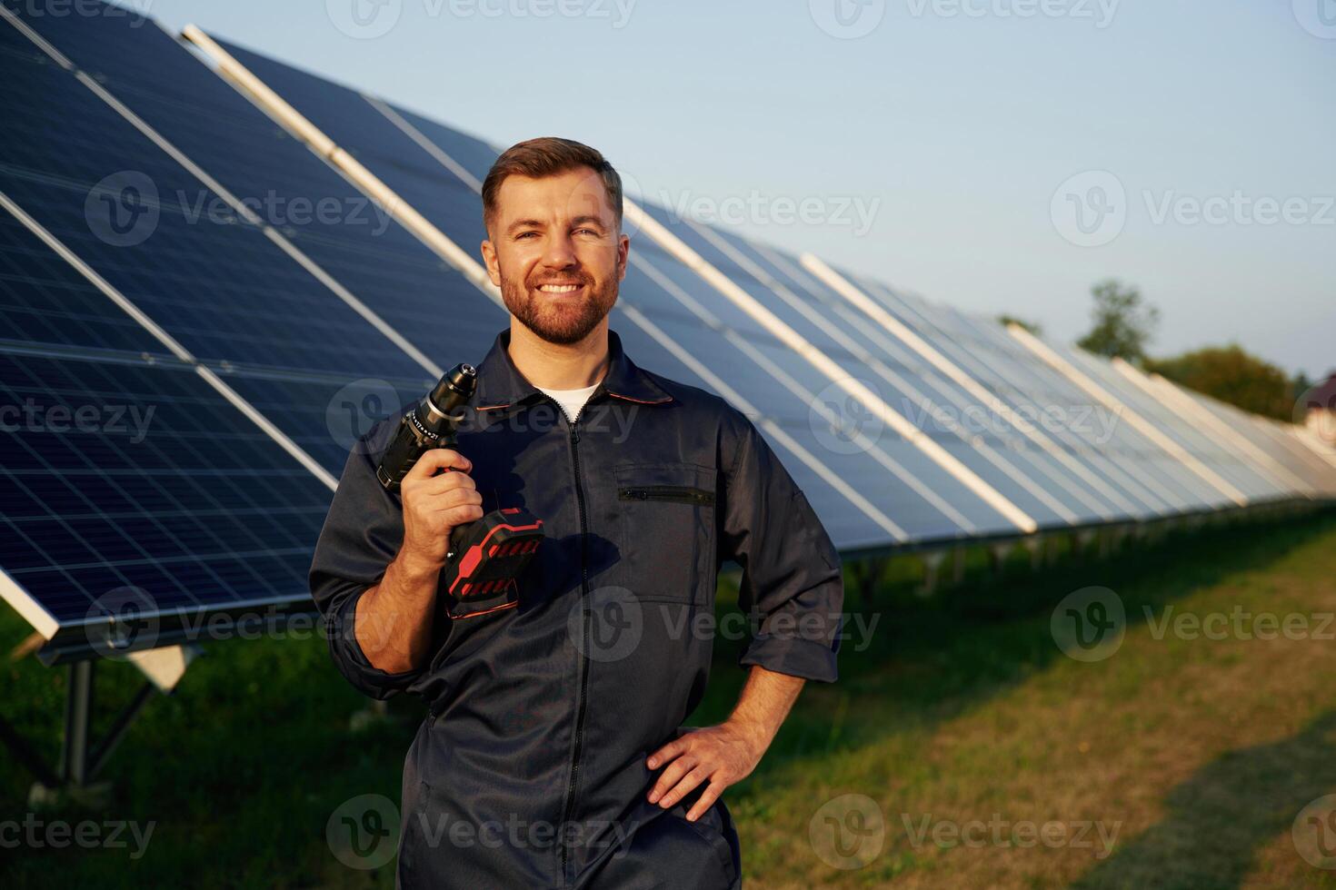 Outside, standing,, and holding the drill. Man is working with solar panels outdoors at daytime photo