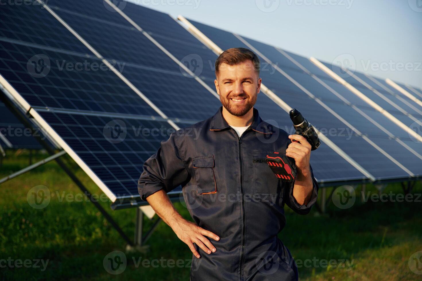 Outside,,, standing and holding the drill. Man is working with solar panels outdoors at daytime photo