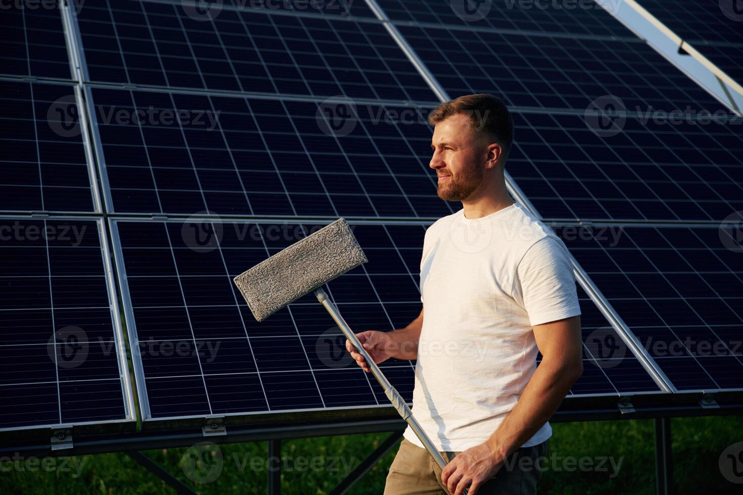 Mop in hands... Man is working with solar panels outdoors at daytime photo