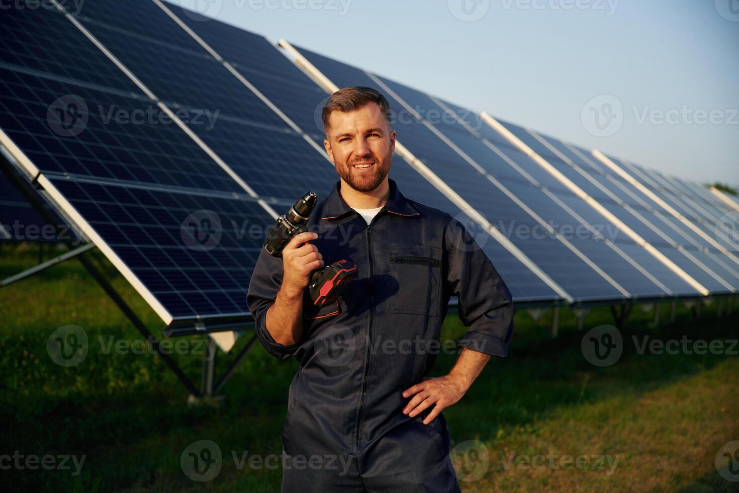 Outside,, standing and holding the drill. Man is working with solar panels outdoors at daytime photo