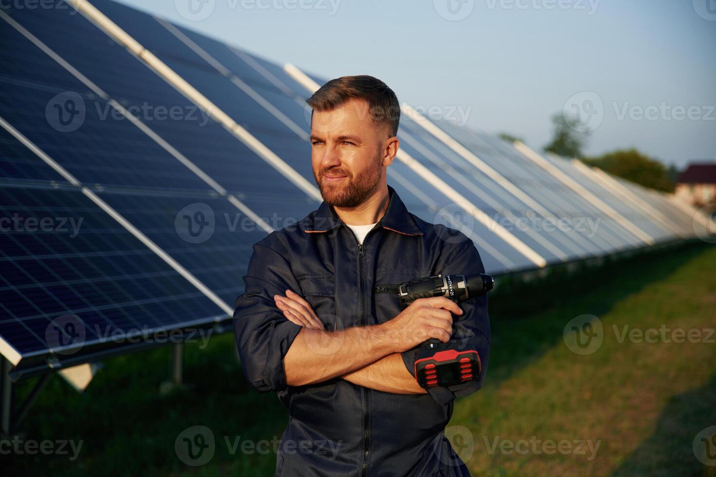 Arms crossed, standing.. Man is working with solar panels outdoors at daytime photo