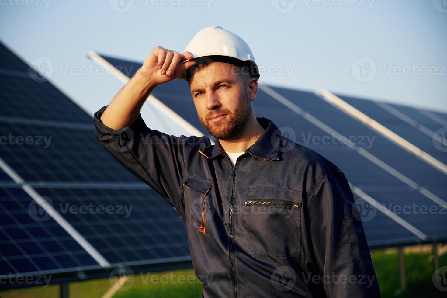 Touching the, white ,hard ,hat. Man is working with solar panels outdoors at daytime photo