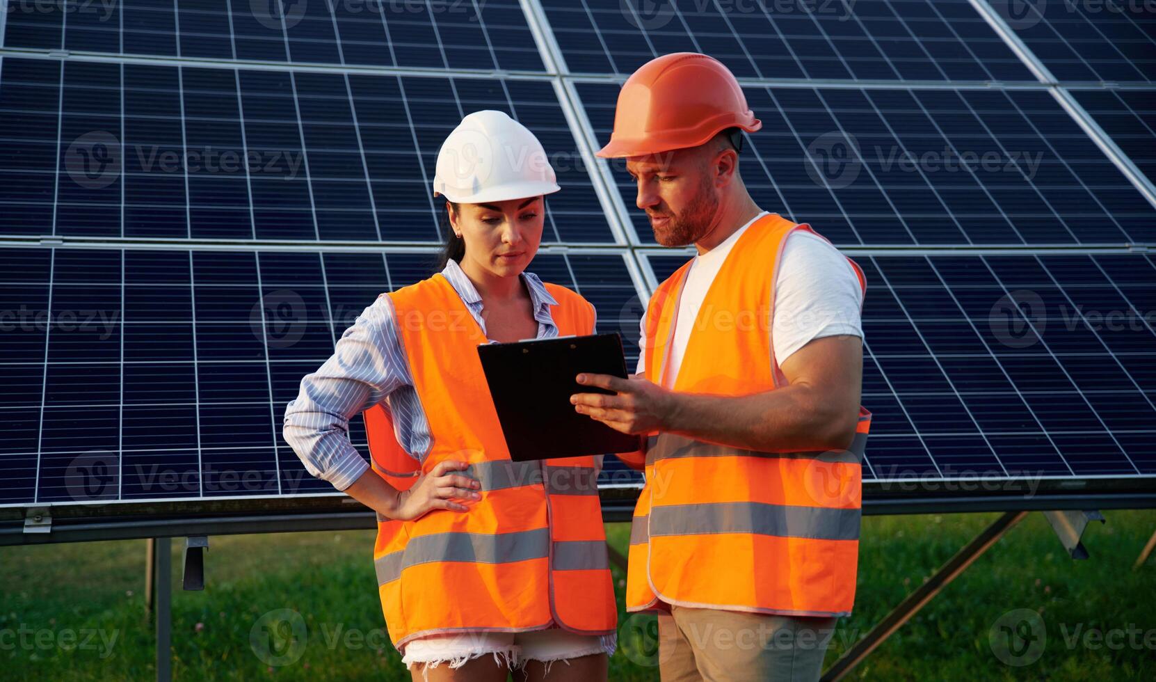 Reading, the ,information ,from notepad. Man and woman, workers are near solar panels, in uniform photo