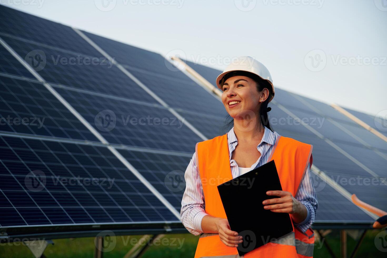 Black notepad ,in ,hands. Female worker engineer in uniform is near solar panels photo