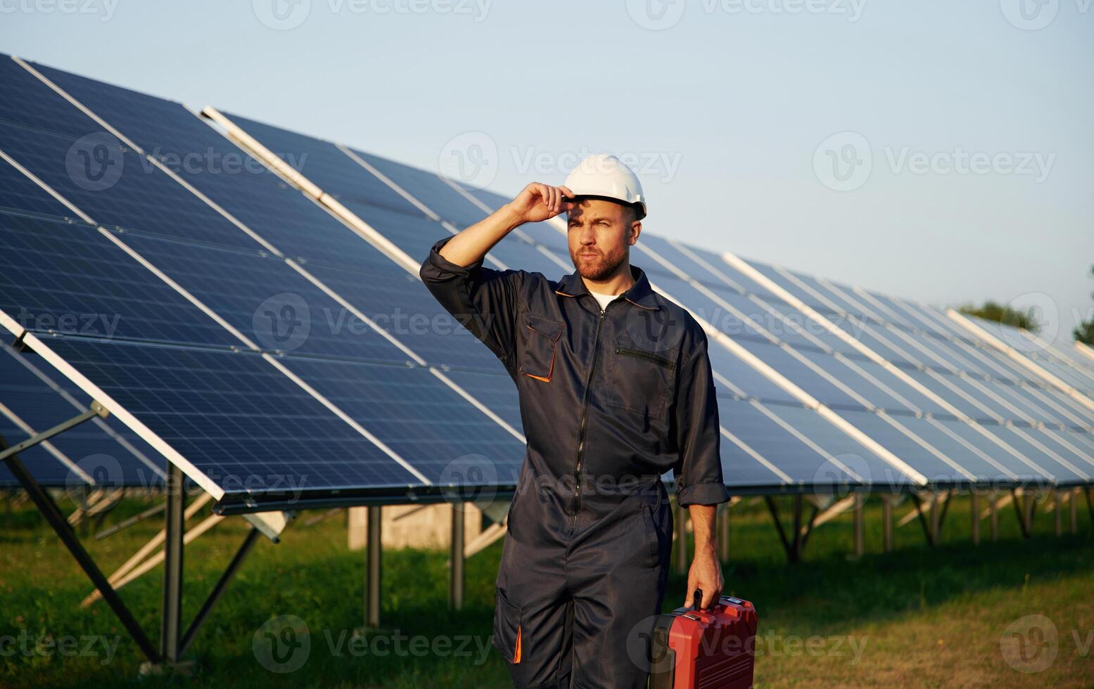 Touching, the white hard hat. Man is working with solar panels outdoors at daytime photo