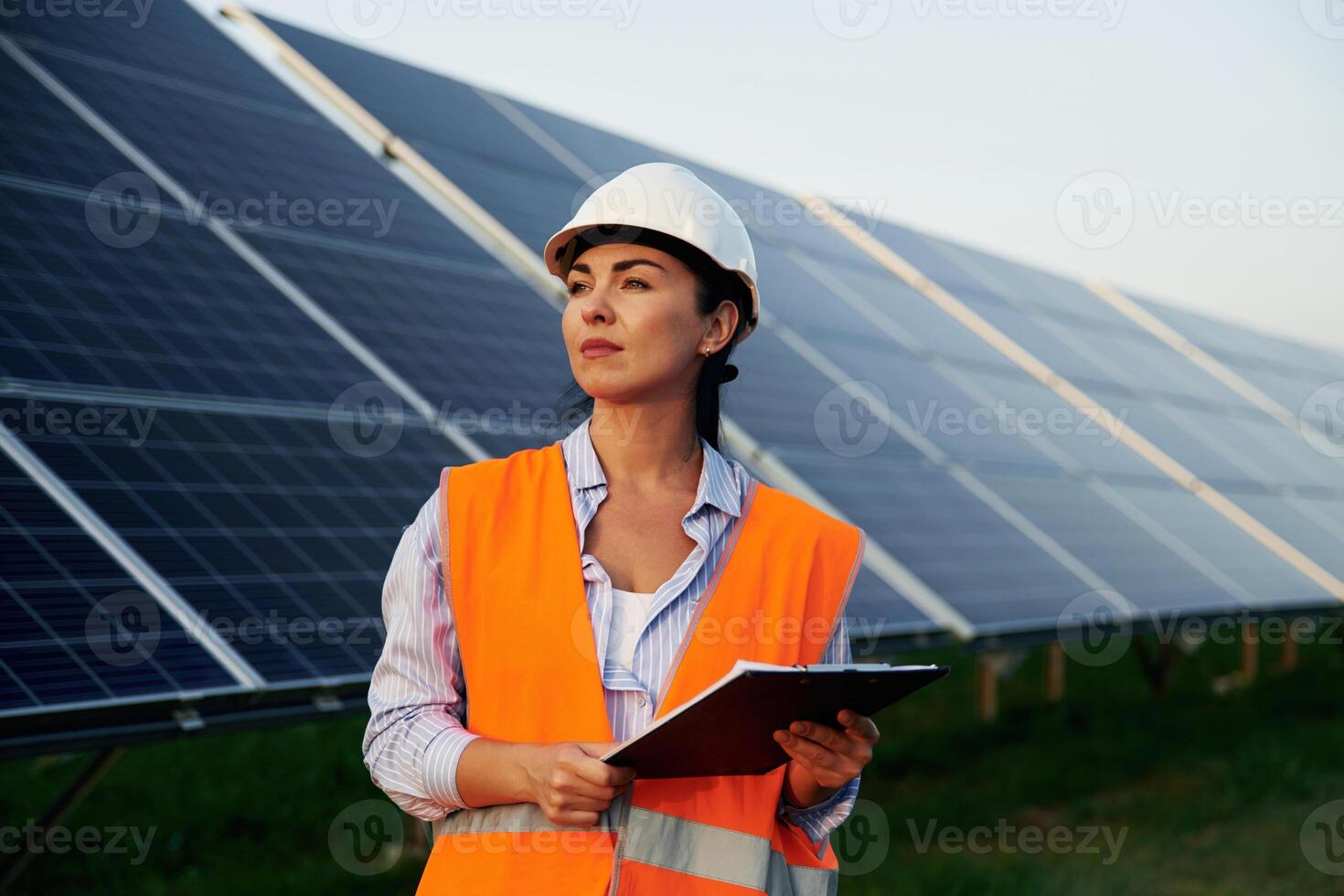 Checking, the data, with notepad. Female worker engineer in uniform is near solar panels photo