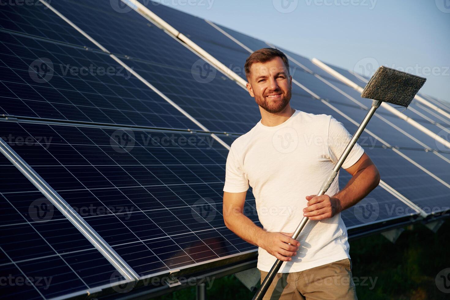 Mop, in hands. Man is working with solar panels outdoors at daytime photo