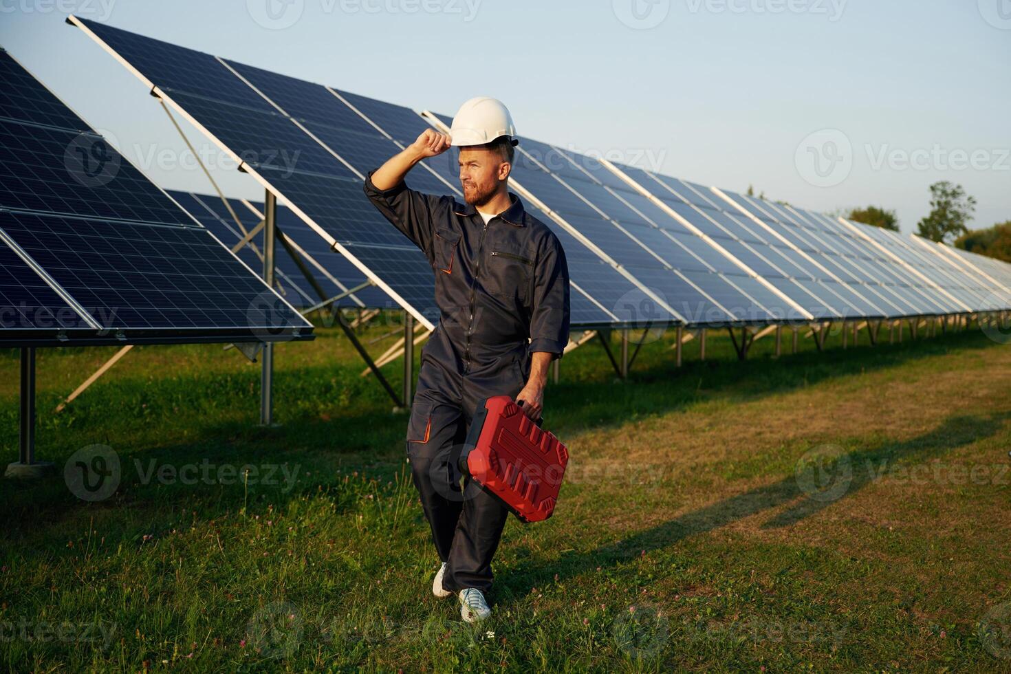 Red, case in hand. Man is working with solar panels outdoors at daytime photo