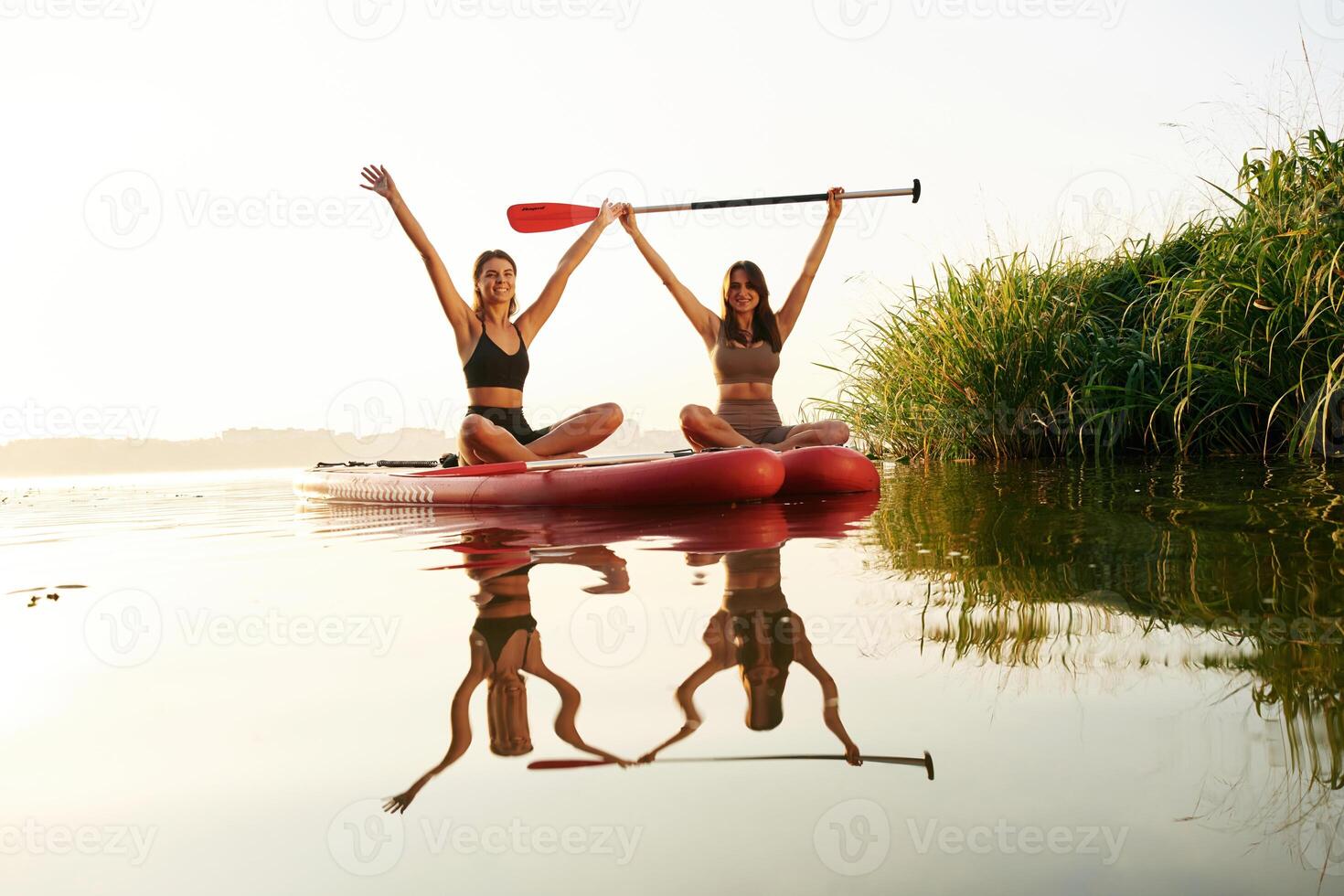 Hands up, smiling and looking,, forward. Women friends are on sup board on the lake together photo