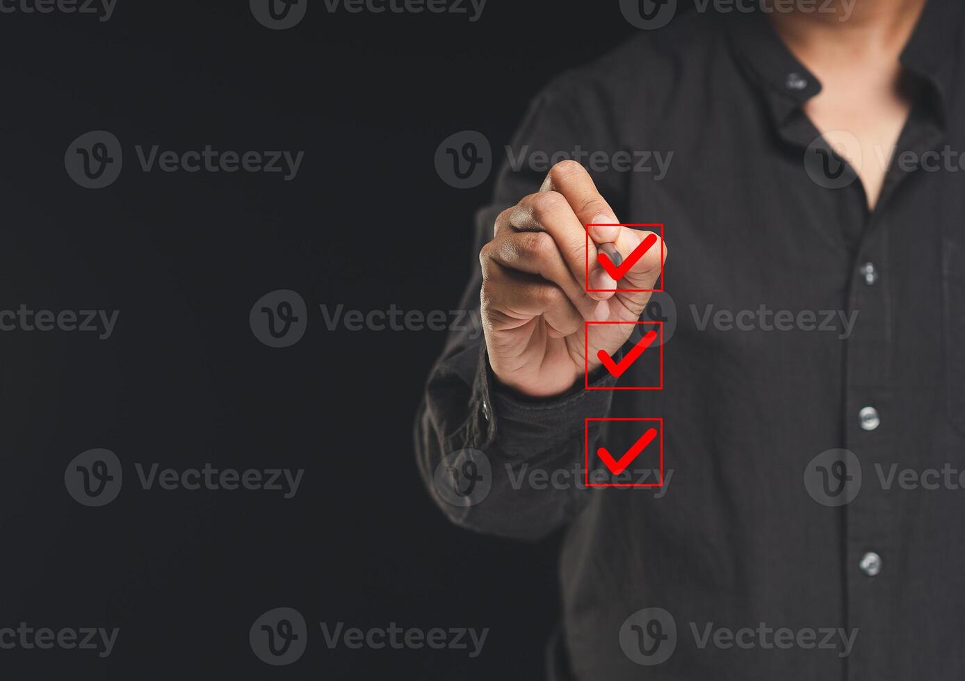 Businessman holding a pen and checking a mark on the boxes symbol is one of three options while standing on a black background. photo