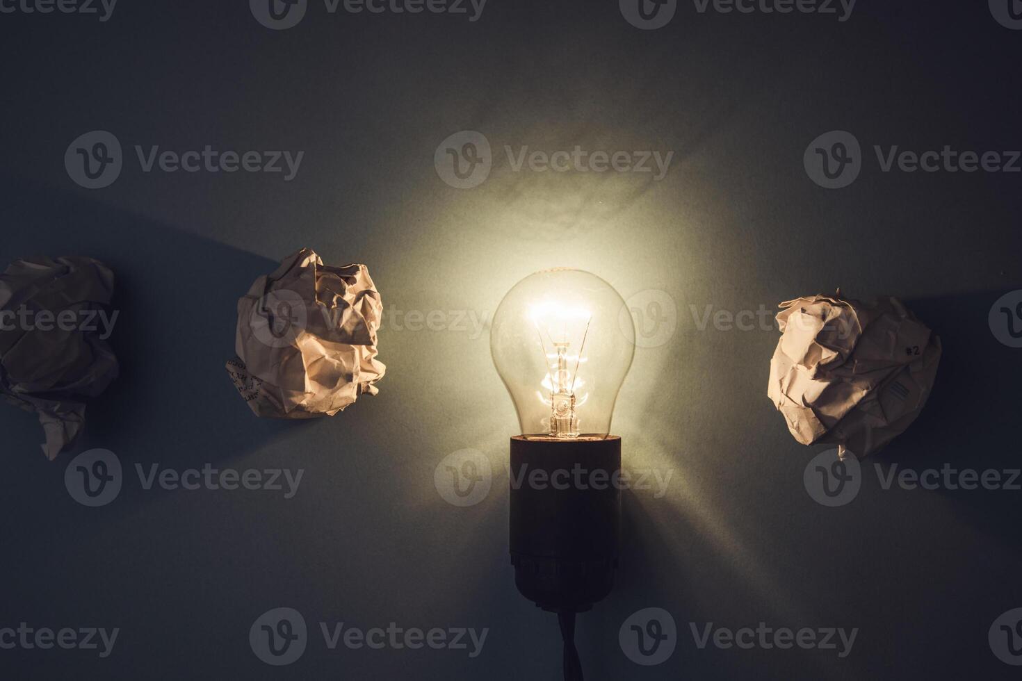 A light bulb is on a wall with three paper sculptures photo