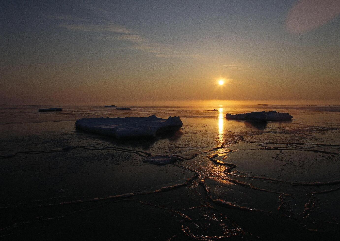a sunset over the ocean with ice floating in the water photo