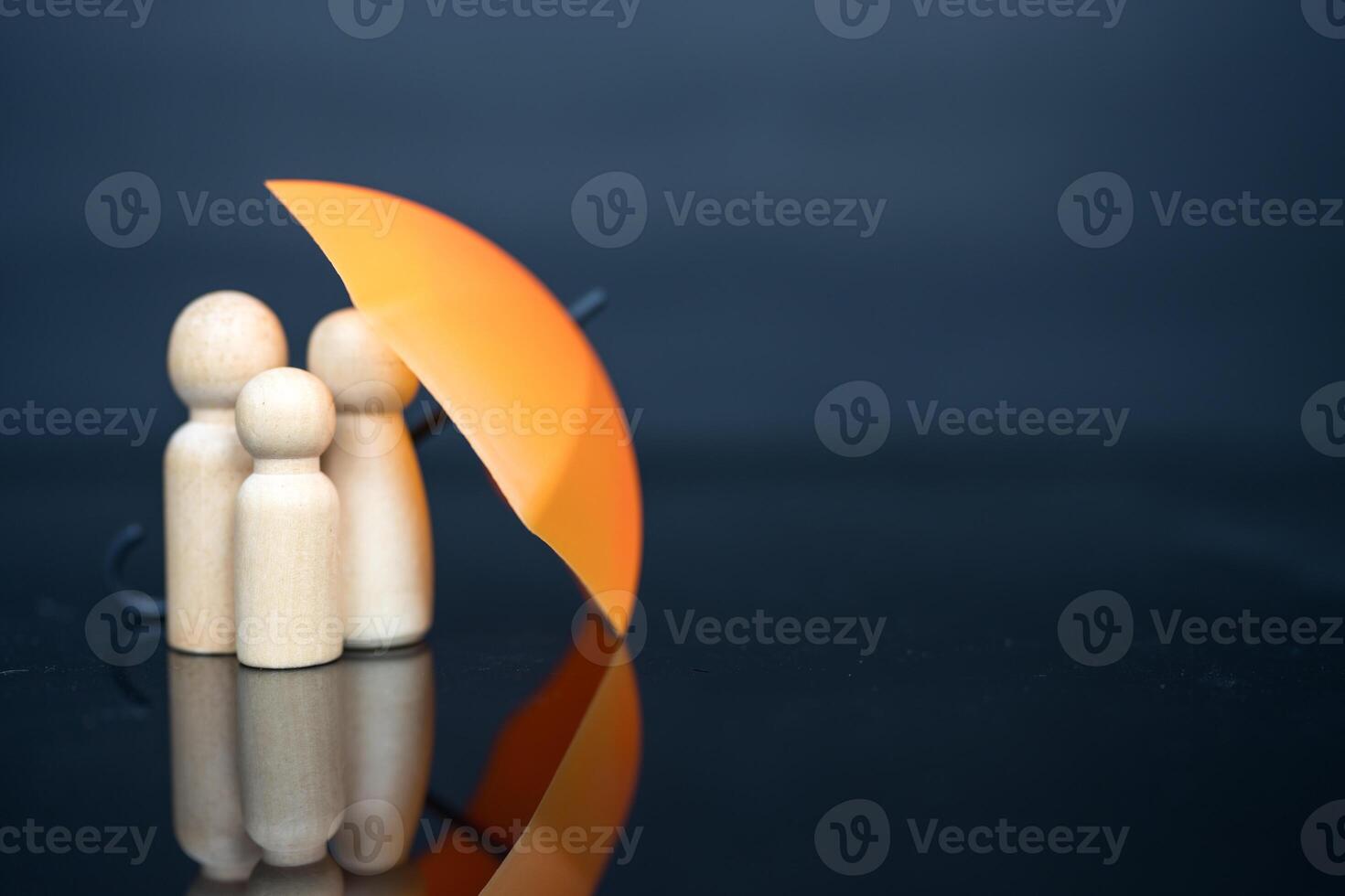 Wooden family peg dolls under an orange umbrella, symbolizing the protective role of insurance in safeguarding families. photo
