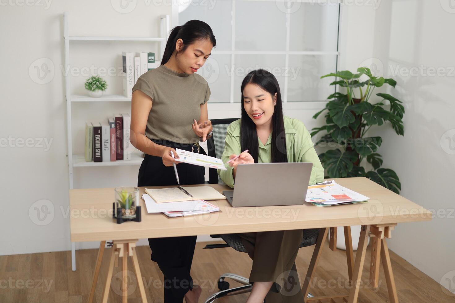 High angle view shot, Asian woman standing holding documents while discussing business ideas and plans with coworker sitting in front of laptop. photo