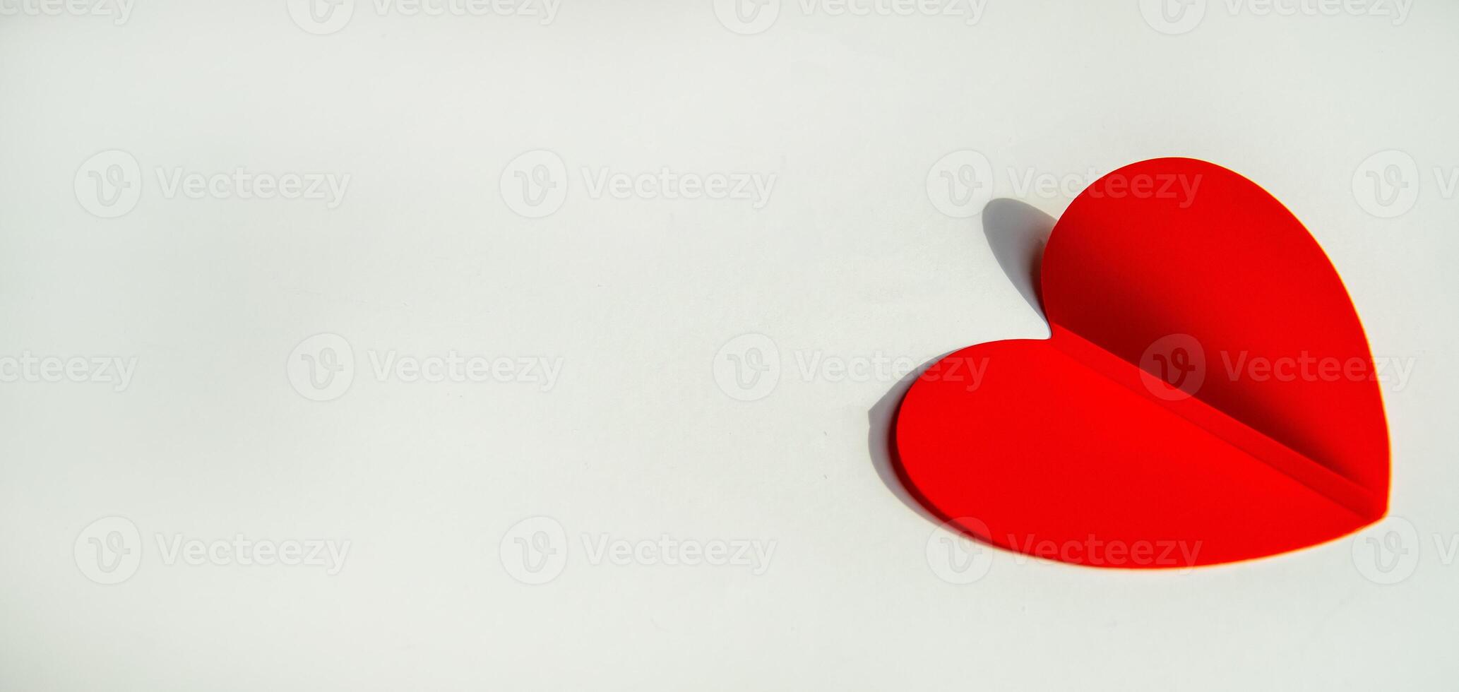 Banner with paper decoration in the shape of a red heart on a white background. Flat plan, top view, space for text on the left side photo