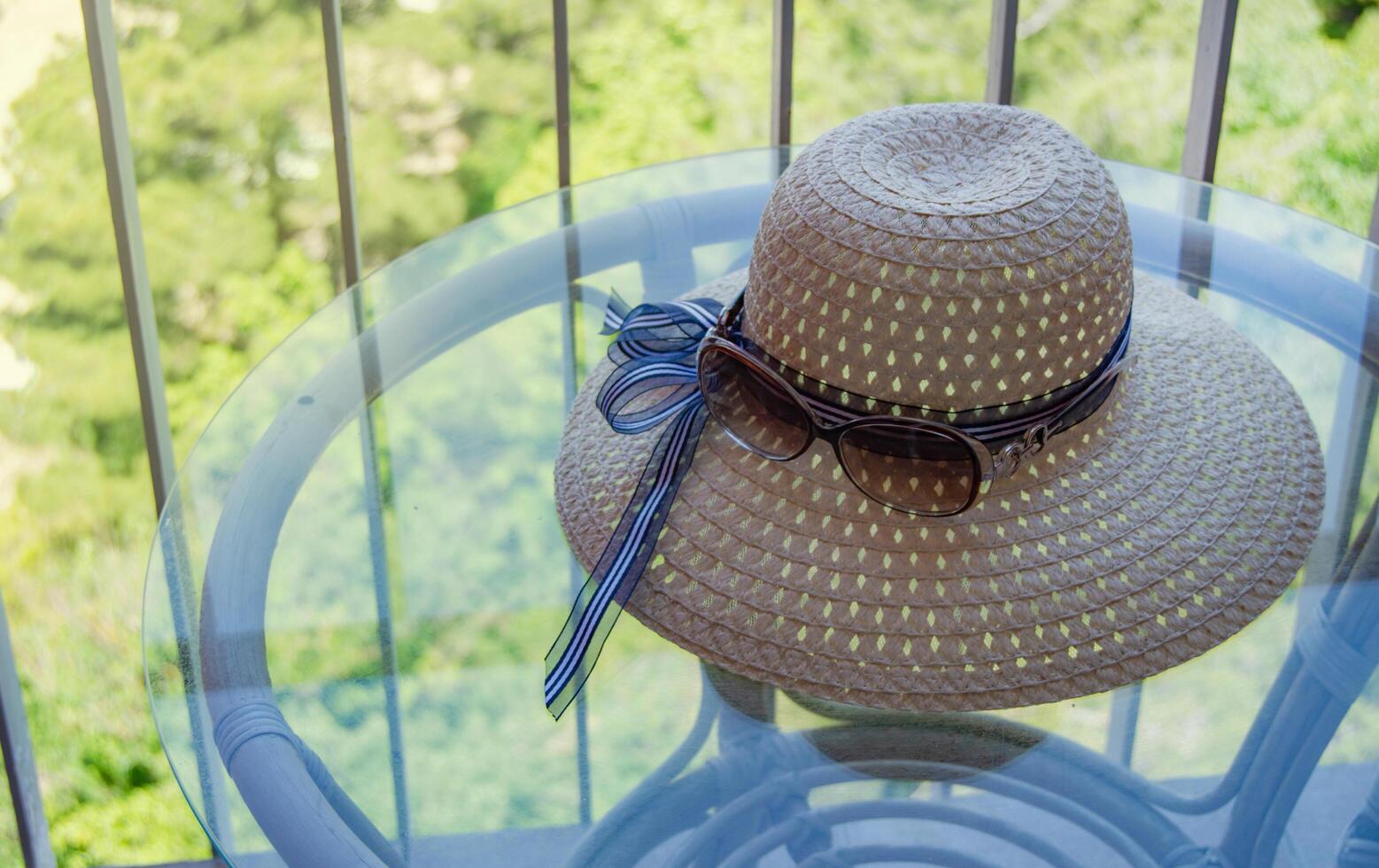 Summer straw hat and sunglasses close-up on a glass table on the balcony photo