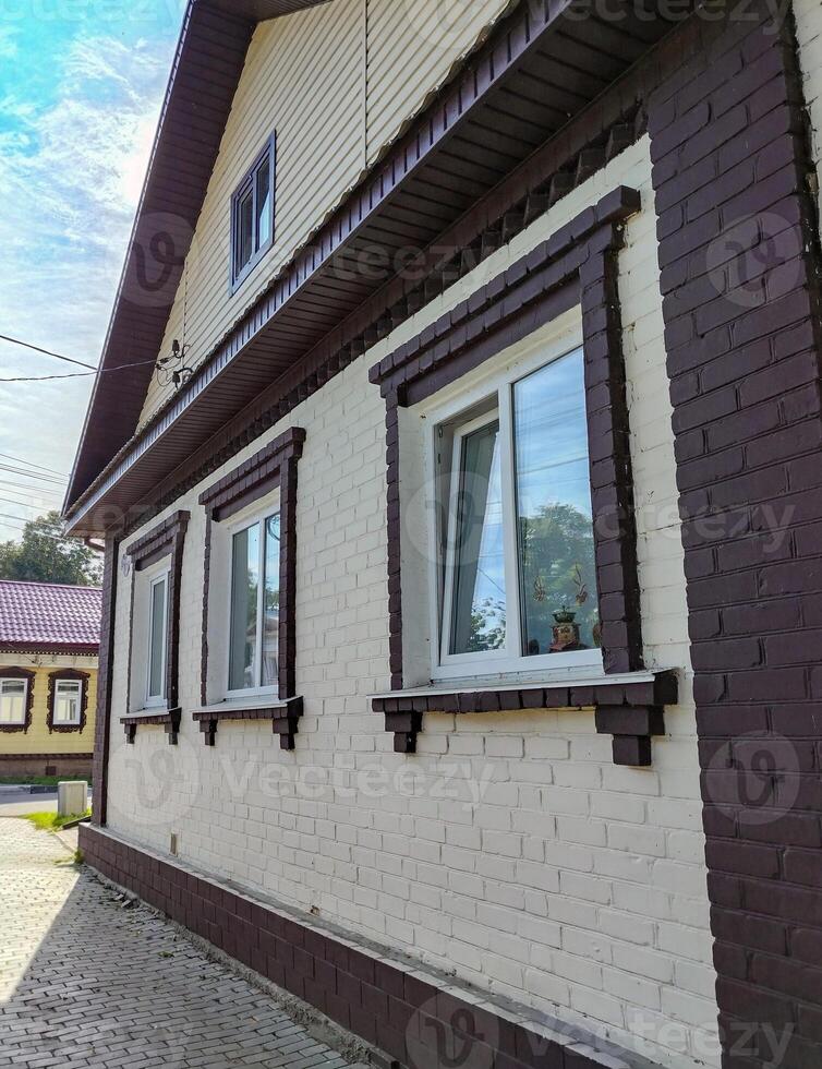 Side view of a one-story brick house with three plastic windows and a gable covered with modern siding photo