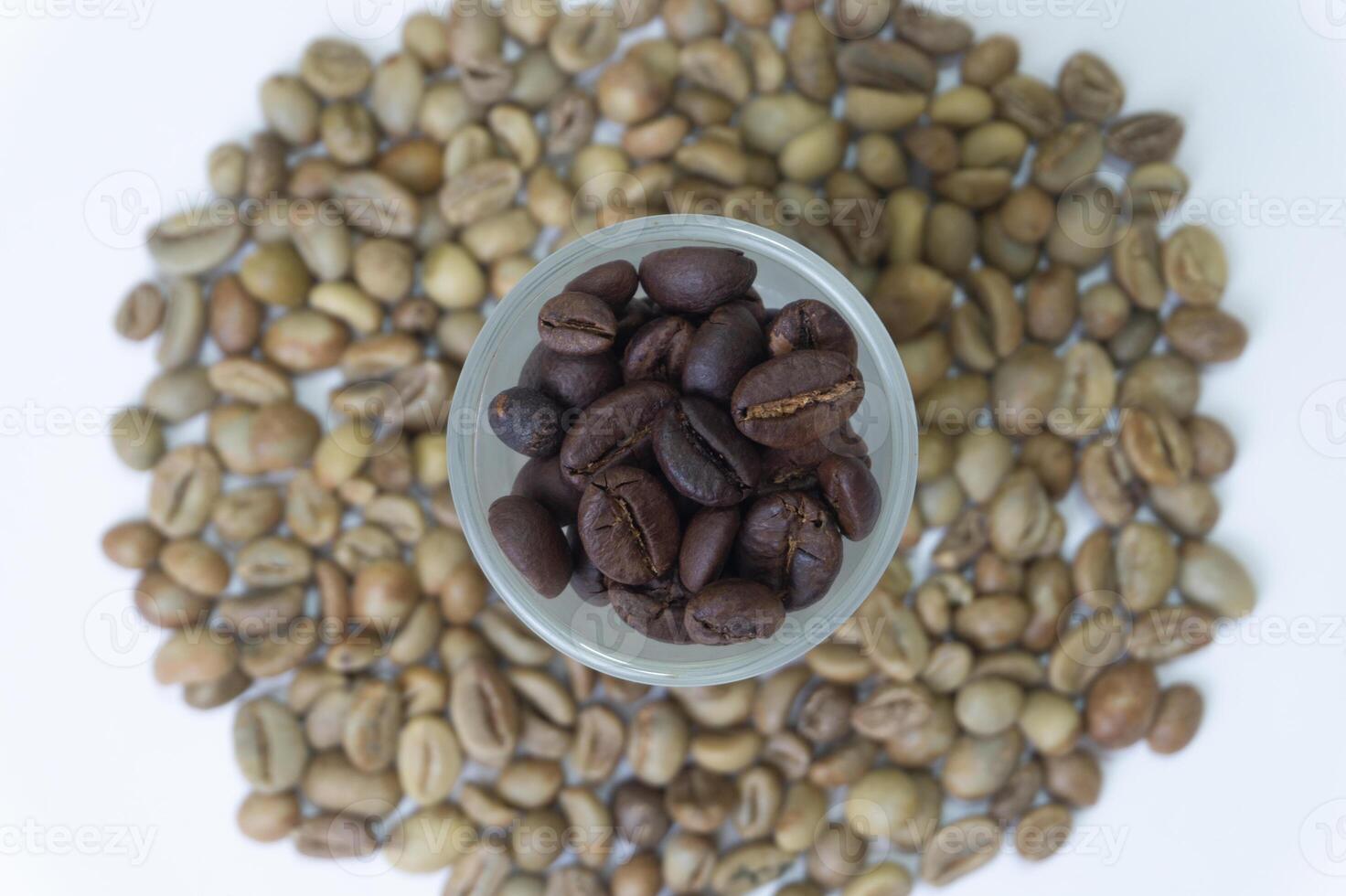 Roasted coffee beans in a glass with unroasted coffee beans in the background photo
