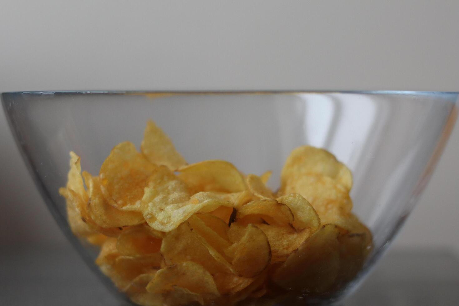 Crispy potato chips in a glass bowl on a neutral background during a casual gathering photo
