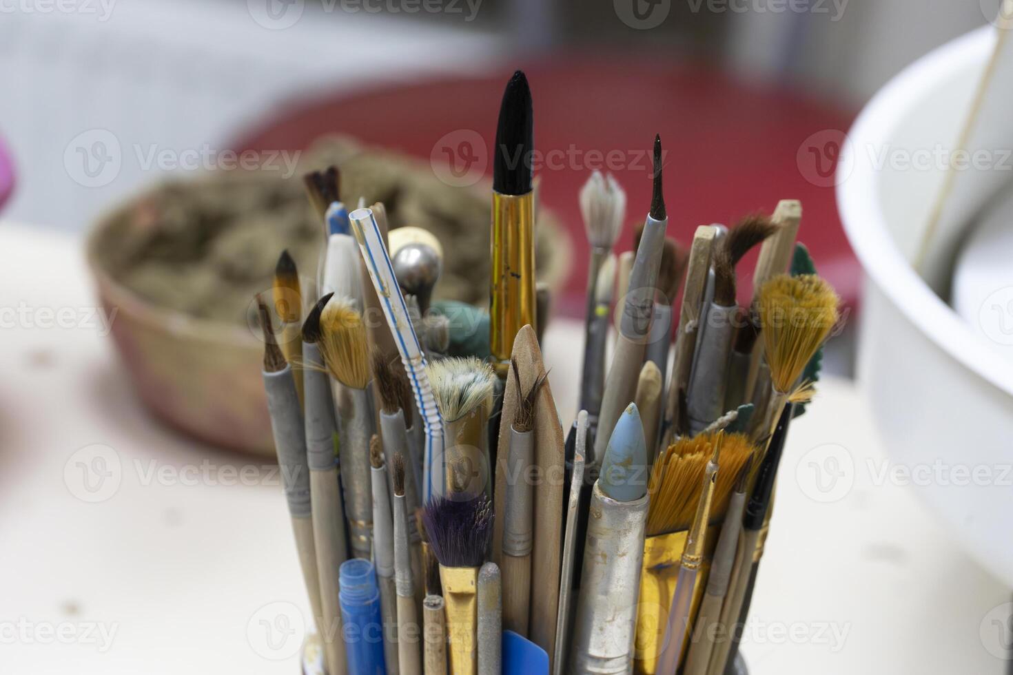 Brushes in Ceramic Cup with Clay on Background in Pottery Studio photo