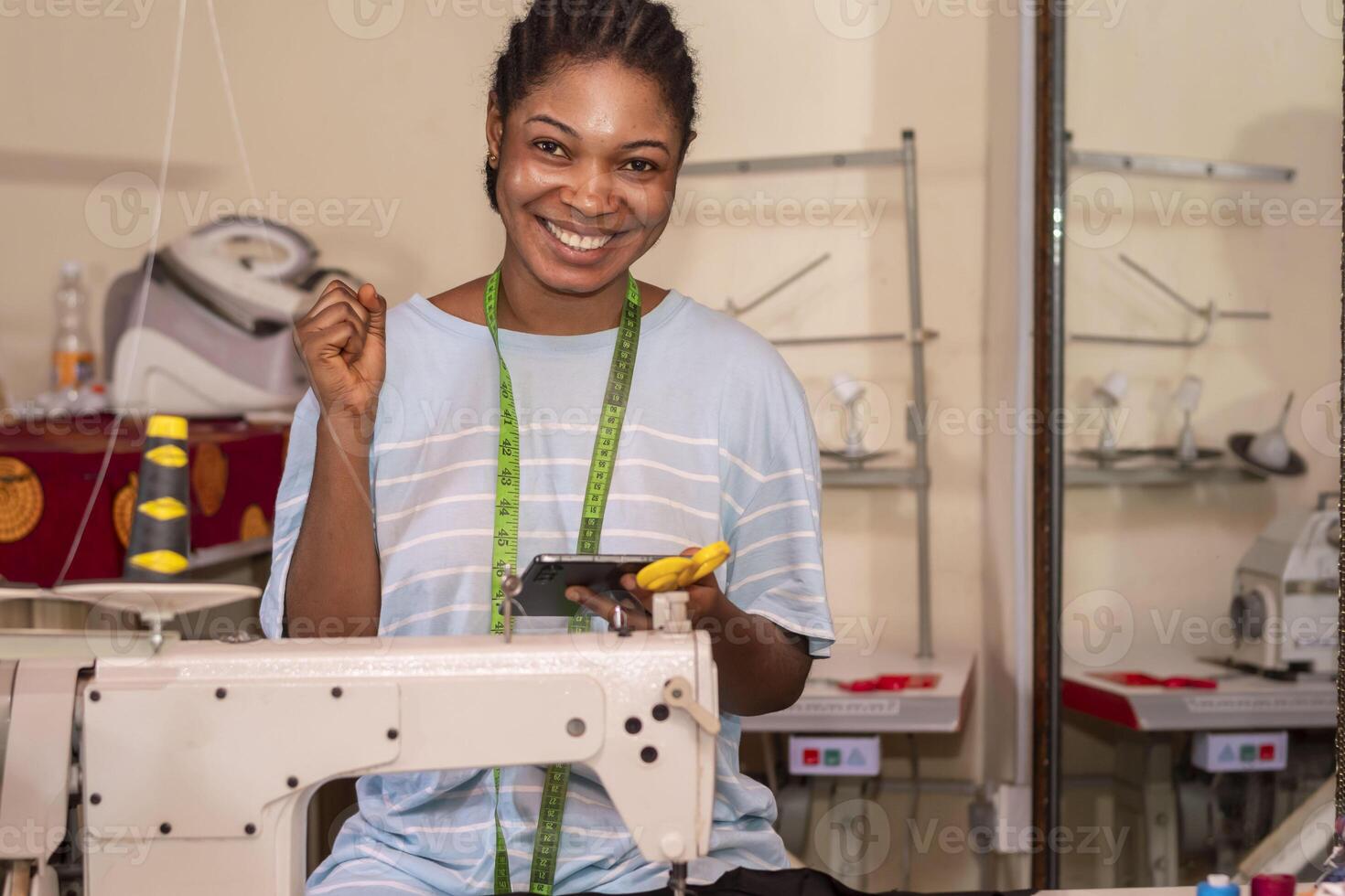 Happy female dressmaker using her phone while working on sewing machine photo