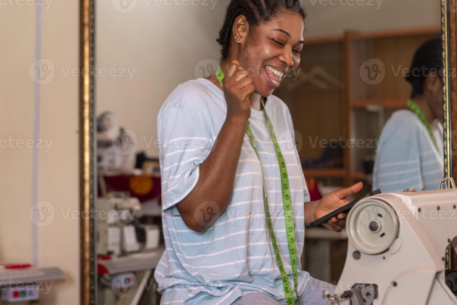excited female dressmaker using her phone while working with sewing machine photo